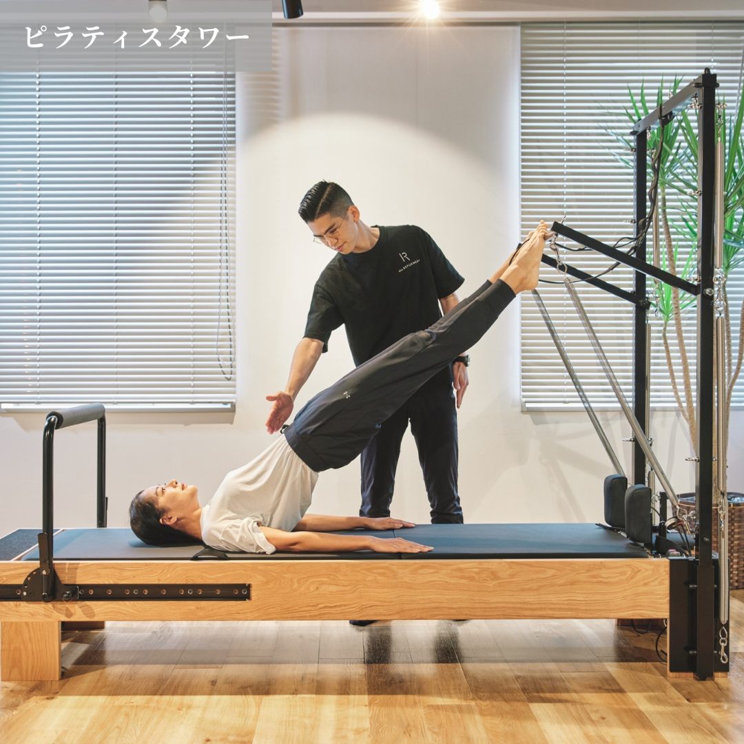 ピラティスタワーで脚を上げるエクササイズをトレーナーが指導する様子
